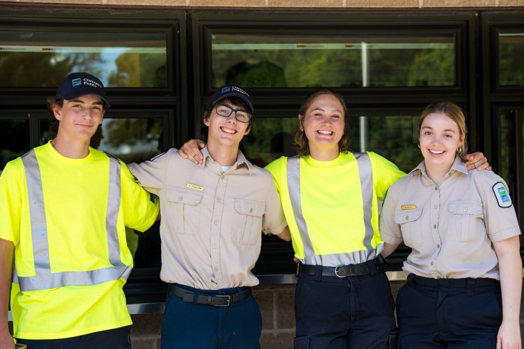 Four smiling staff members, some in a maintenance uniform, some in an office uniform, with their arms around each other