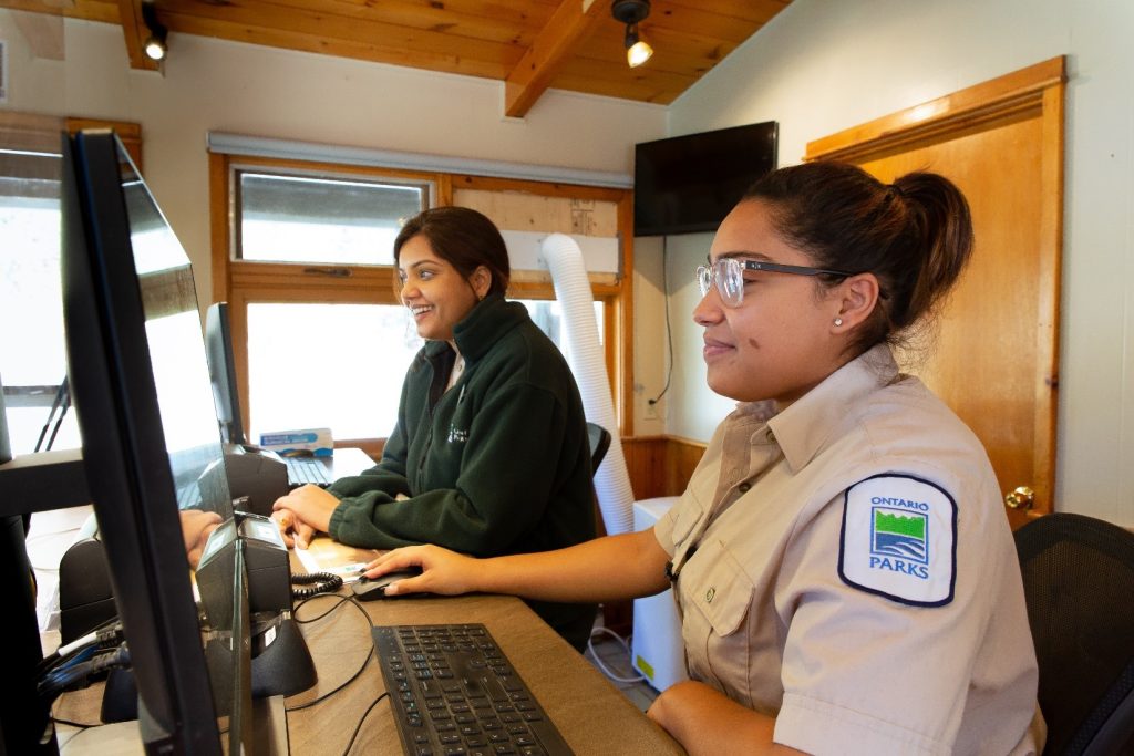 Two smiling gate attendants seated in an office at their computers