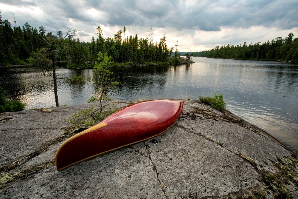 canoe resting overturned on rock, lake surrounded by trees in background