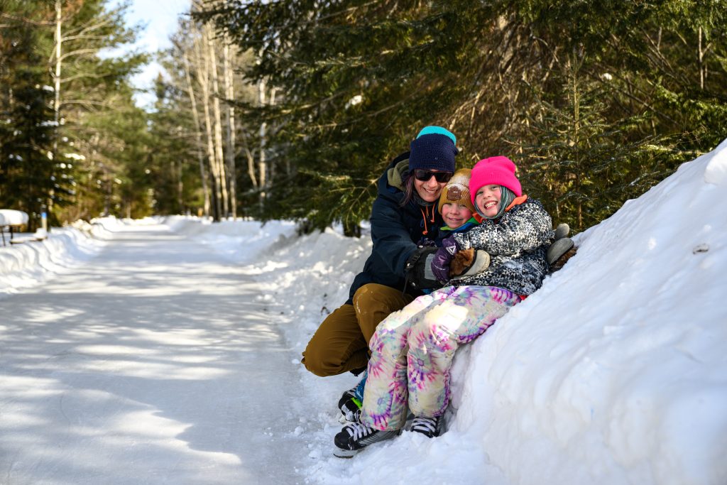 mother and children sitting on snowbank beside skating trail