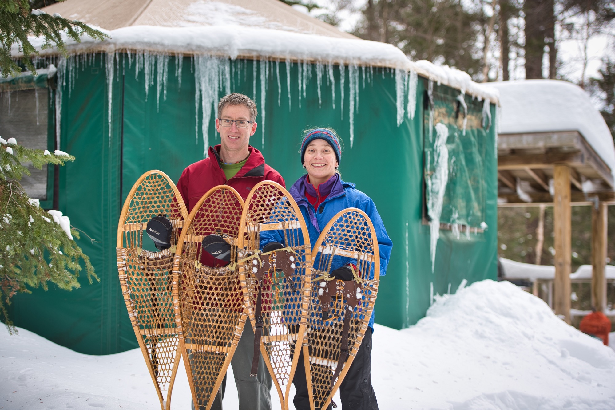 Two people holding snowshoes standing in front of a snow-covered yurt