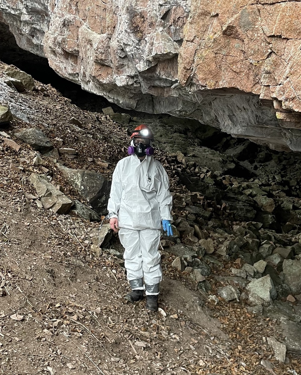 staff wearing respirator, standing near rock formation