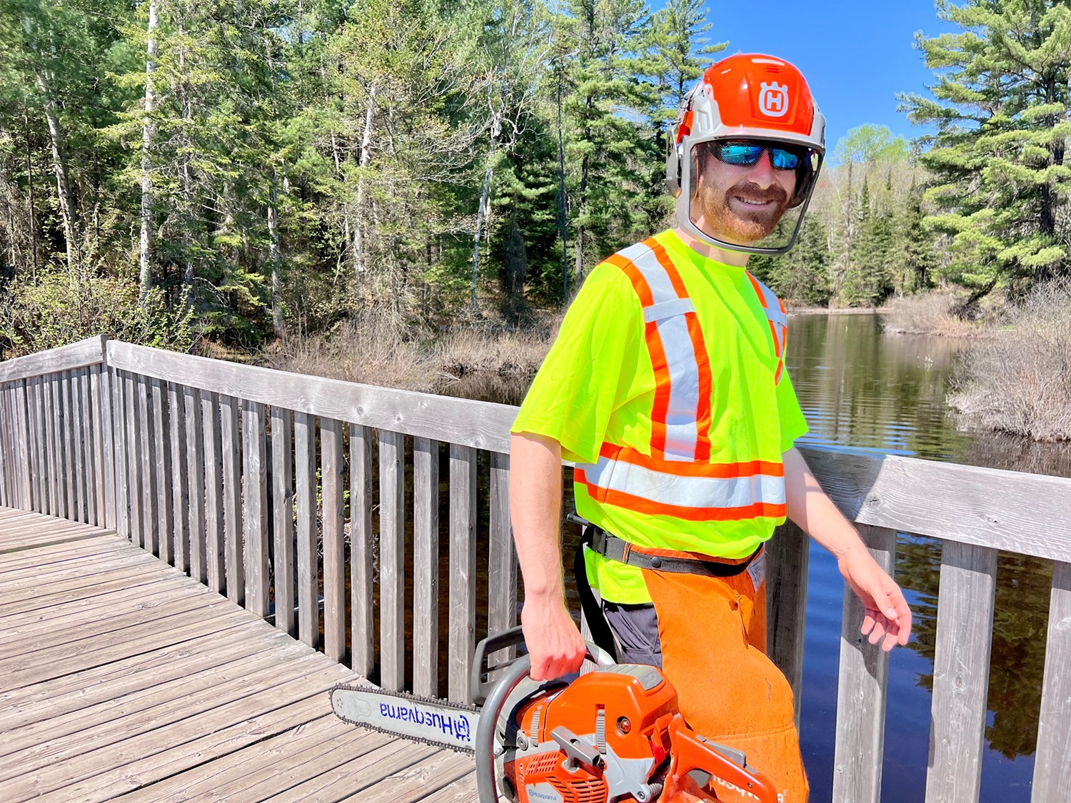 staff holding chainsaw, walking on boardwalk
