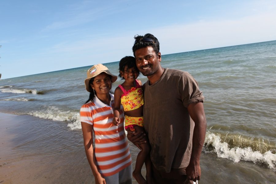 Family of three, on a beach, smiling at the camera, on a sunny day with the water at their backs