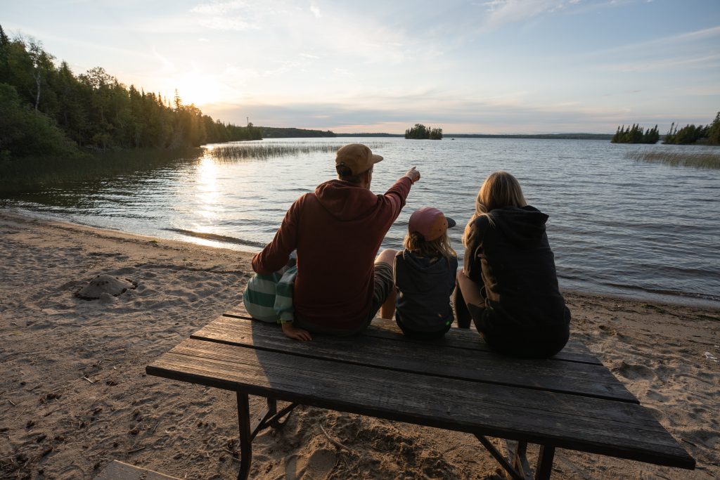 family sitting on picnic table watching sunset over lake