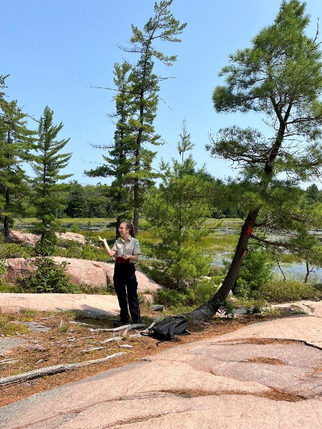 Ontario Parks staffer giving a guided hike on the shores of Killarney Provincial Park, trees and water in background