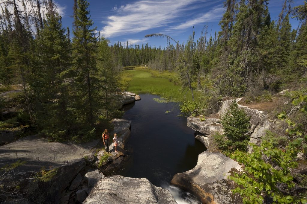 two hikers on large rocky geological feature near river