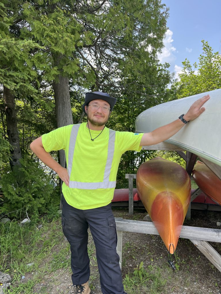 Aadan wearing high vis, standing next to canoes