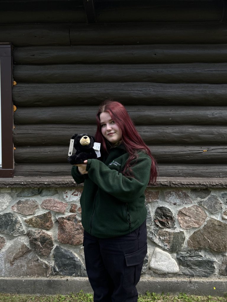 Amber standing outside of park building holding Black Bear plushie