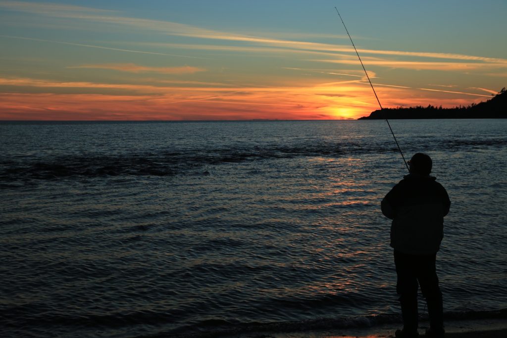 Pêcheur pratiquant la pêche sur la rive du lac Supérieur au crépuscule.