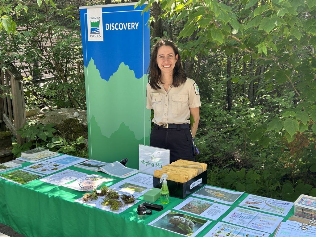 Membres du personnel des programmes Découverte du parc se tenant autour d’une table interactive présentant des photos, des échantillons et des informations sur les mousses.