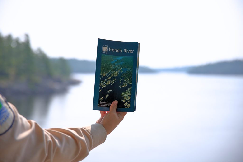 hand holding French River map in front of body of water
