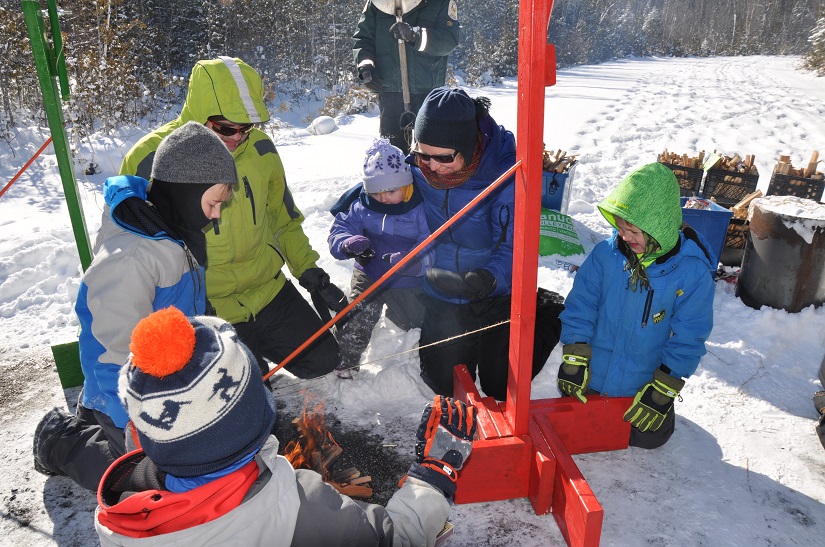 family in snowsuits around campfire