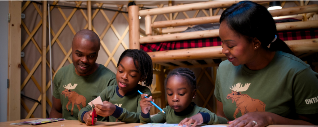 Family doing arts and crafts in a yurt wearing matching pajamas. 