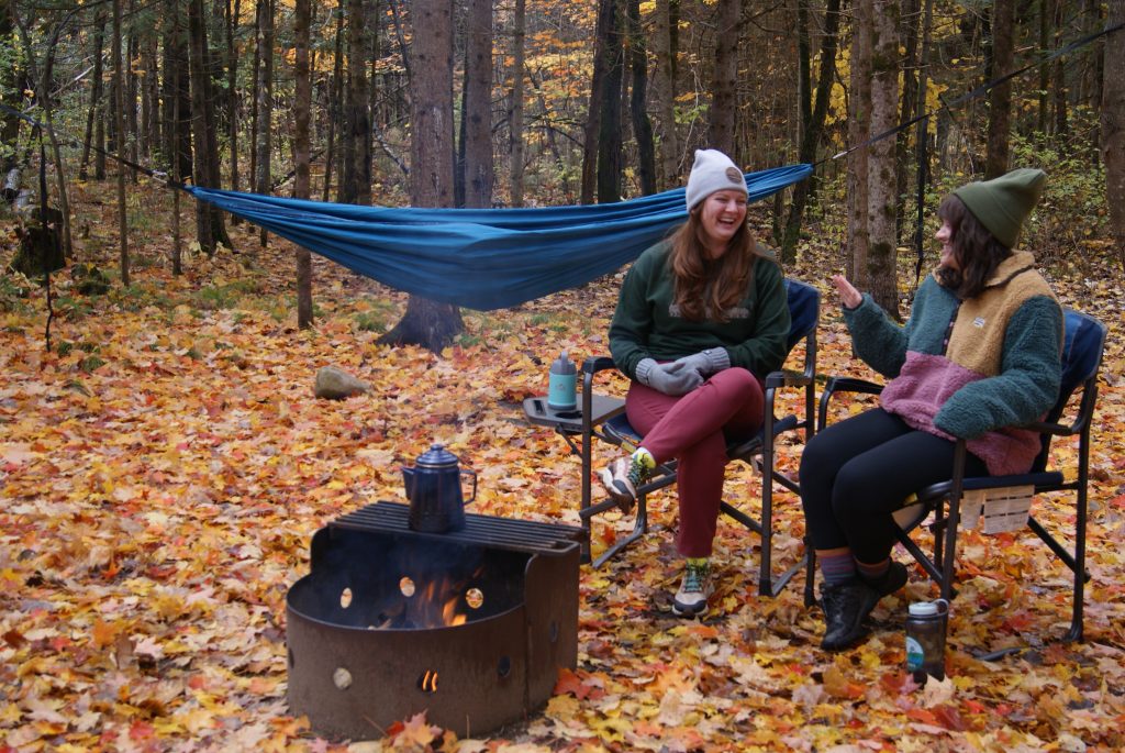 Two people laughing at campsite by a campfire in the fall season
