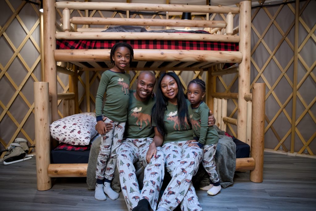 Family wearing matching pajamas sitting on a log bunk bed in a yurt. 
