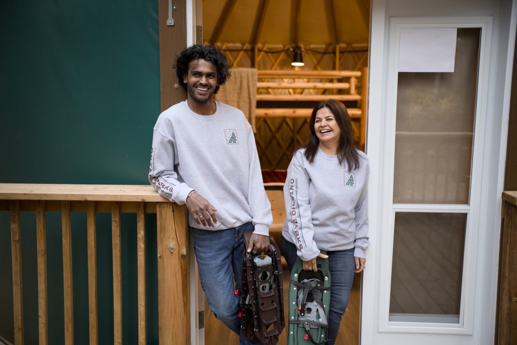 Two people standing in a yurt doorway holding snow shoes. 