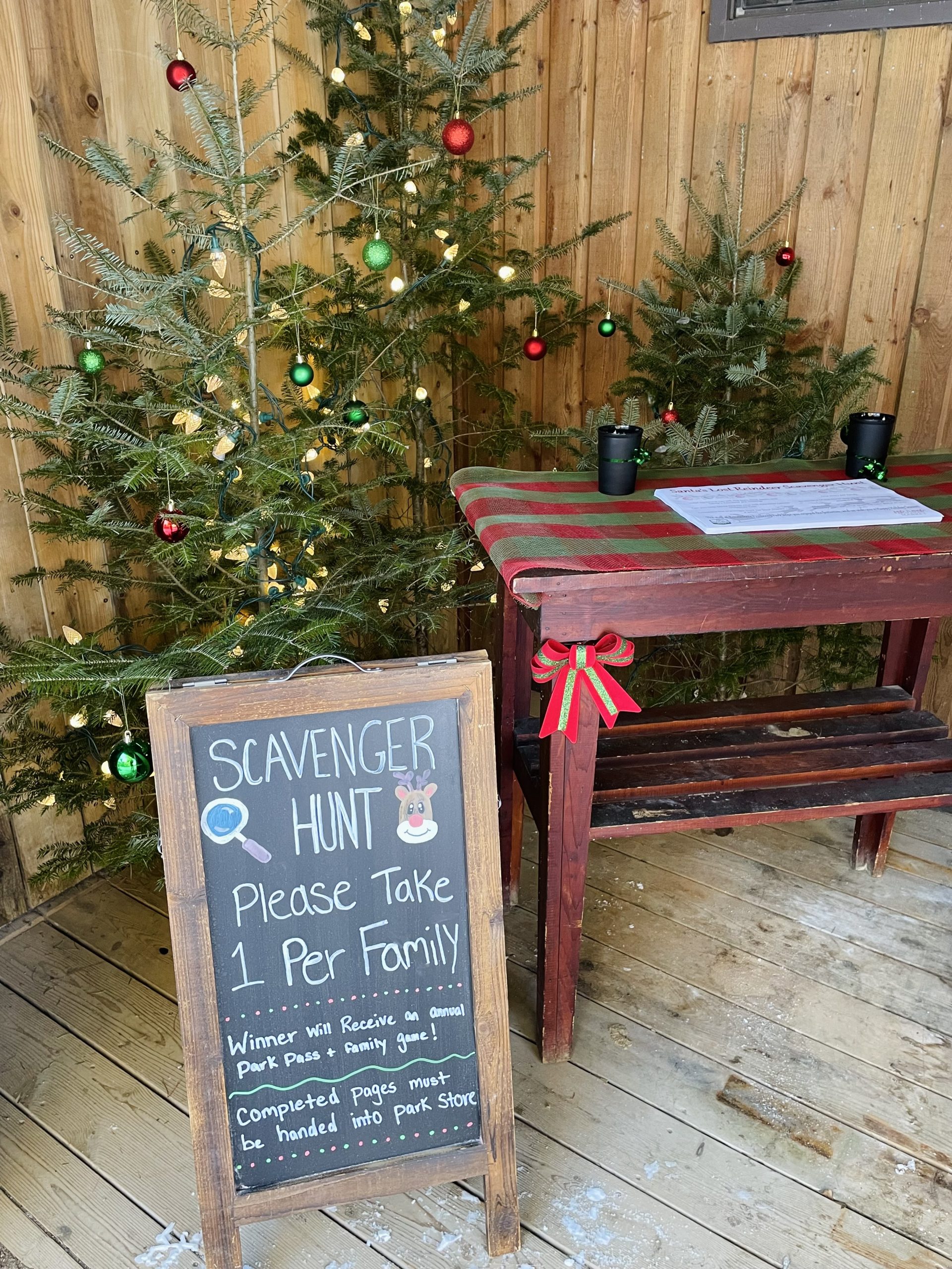 A sign for a holiday scavenger hunt with Christmas trees in the background