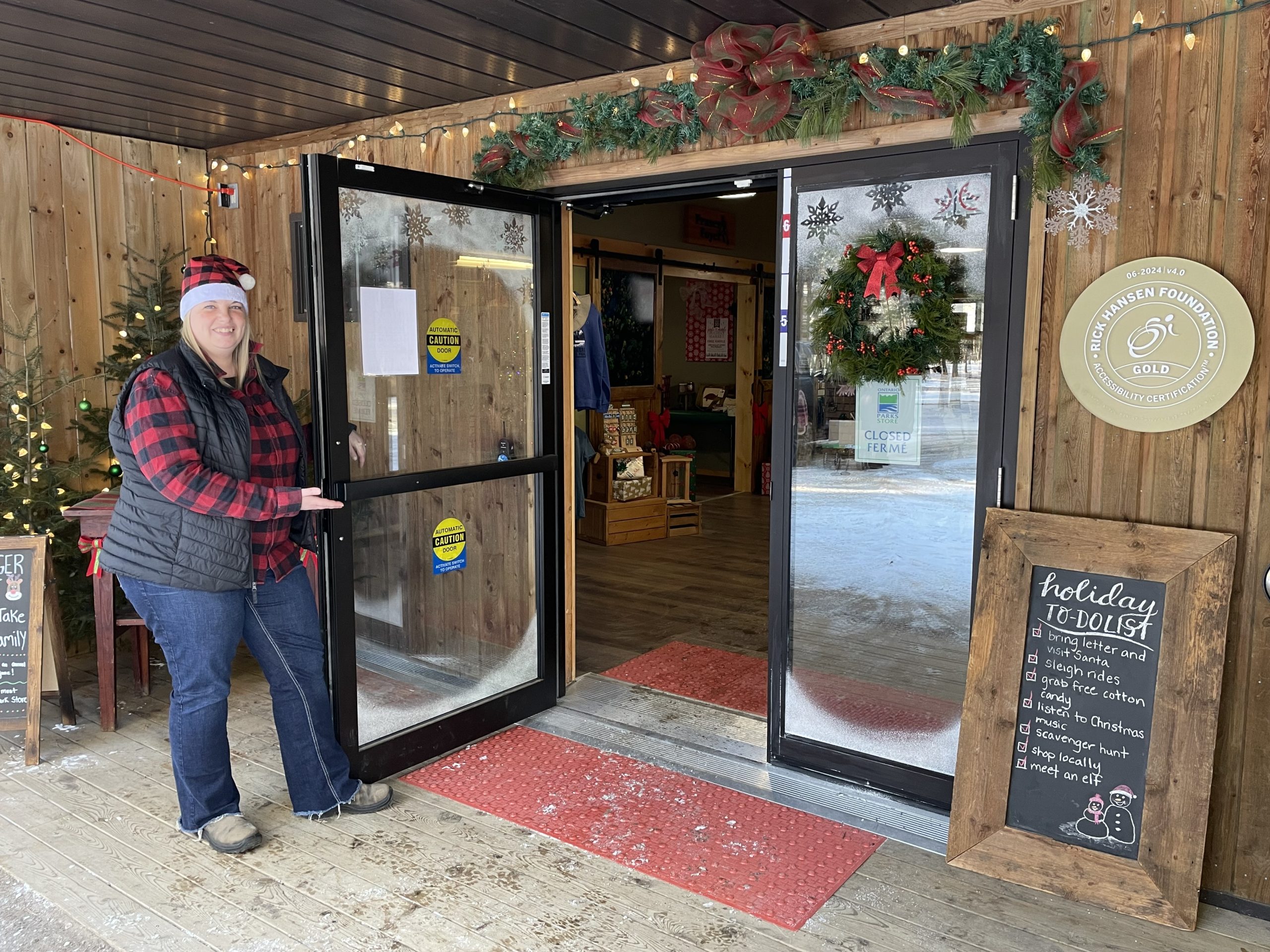 Person in holiday gear holding open the door to decorated park store