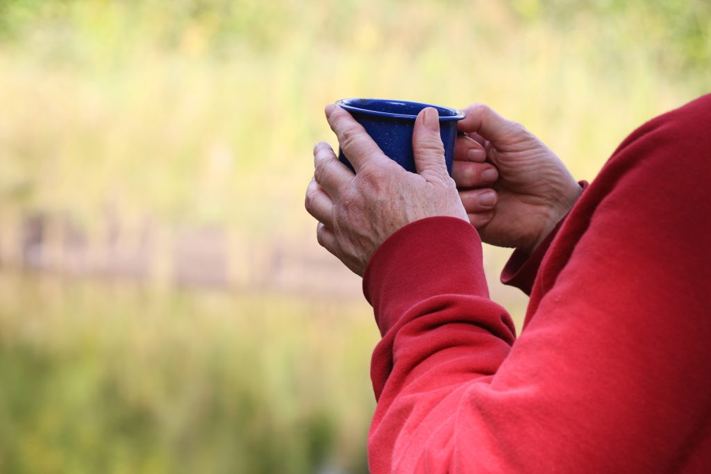 Closeup of someone’s hands holding a hot beverage in nature.