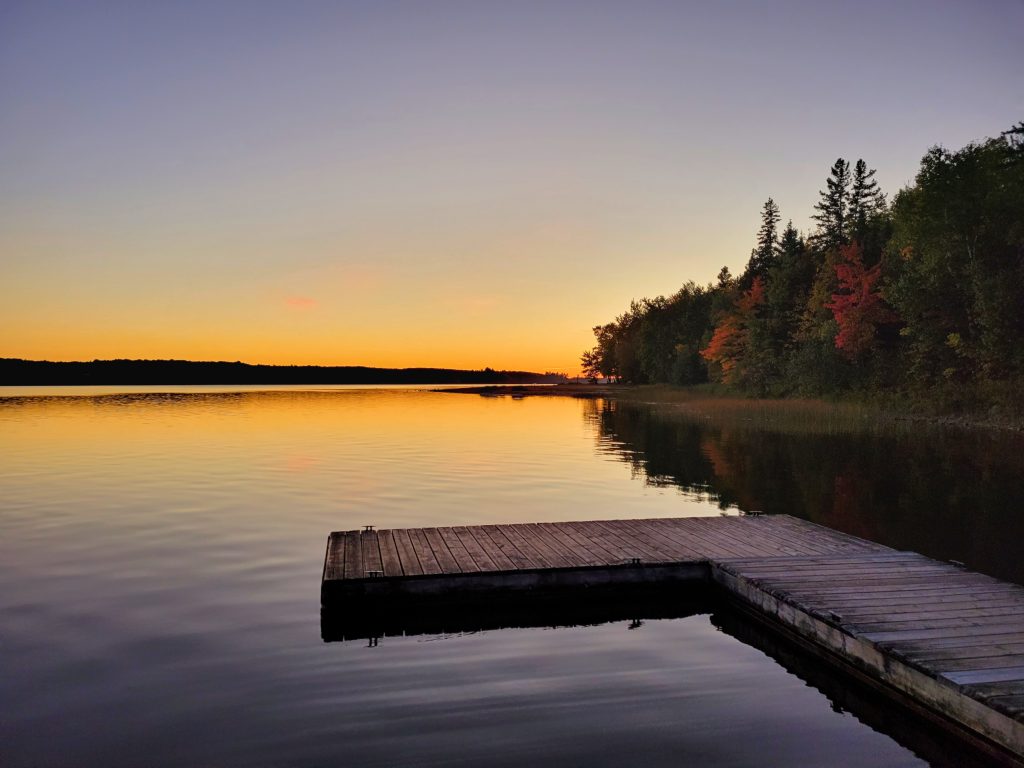 Sunset over a dock on a lake surround by fall trees.
