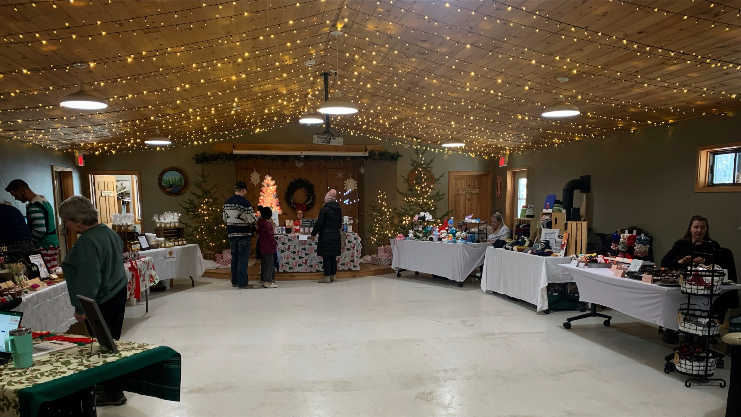 a room with holiday vendor tables, with sparkly lights strung from the ceiling