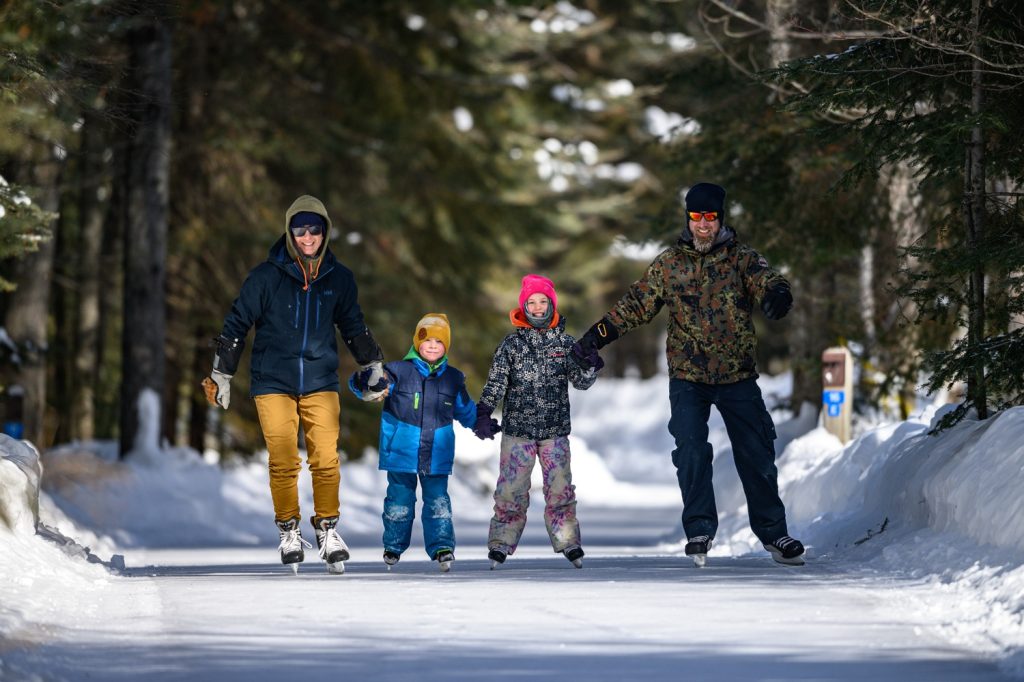 family holding hands and skating on forest ice trail,