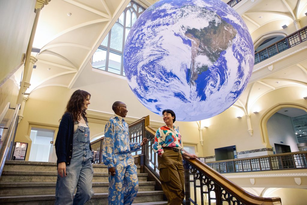 three visitors walking down steps of museum. Large globe hanging from ceiling