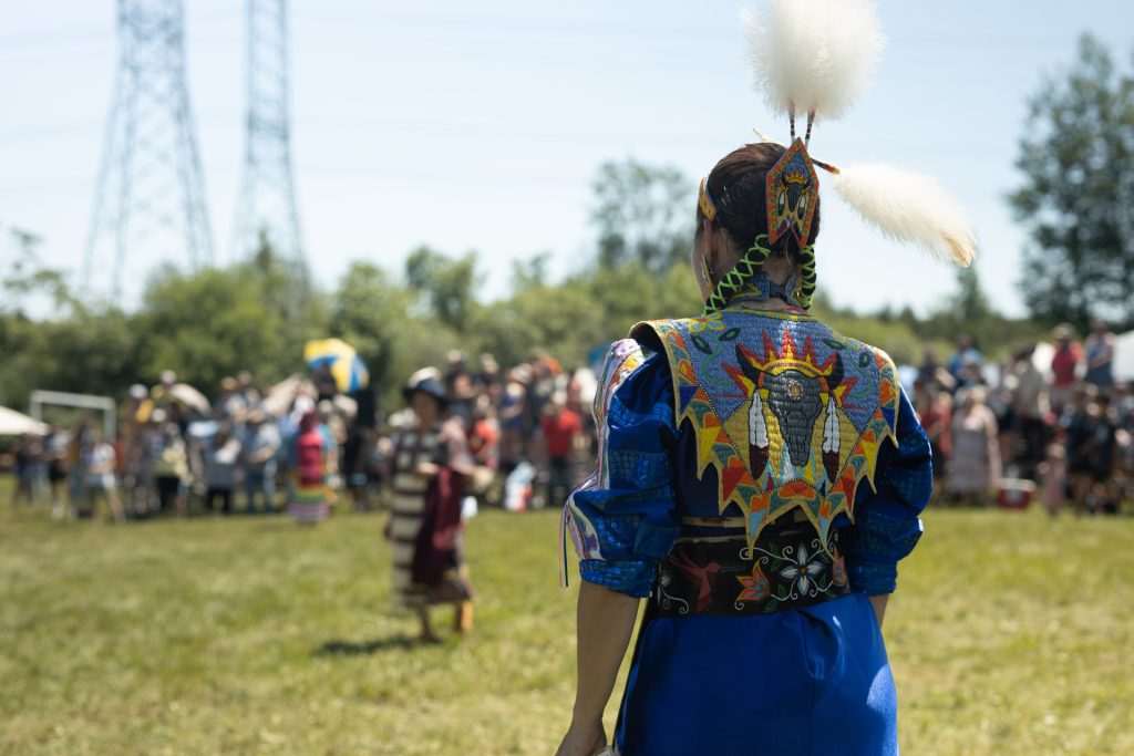 person in traditional Indigenous regalia in foreground, group of people in background