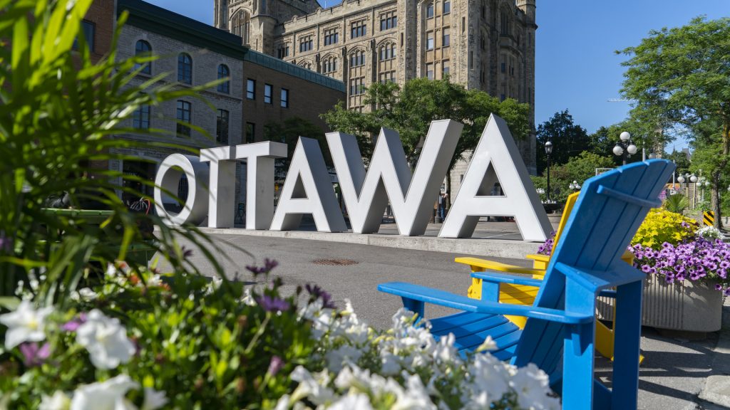 Large "Ottawa" sign in downtown, potted florals and muskoka chairs in foreground