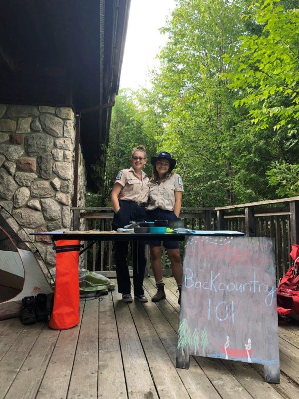 Jordan and Kelly, standing behind a table, running a Discovery Program about backcountry camping.