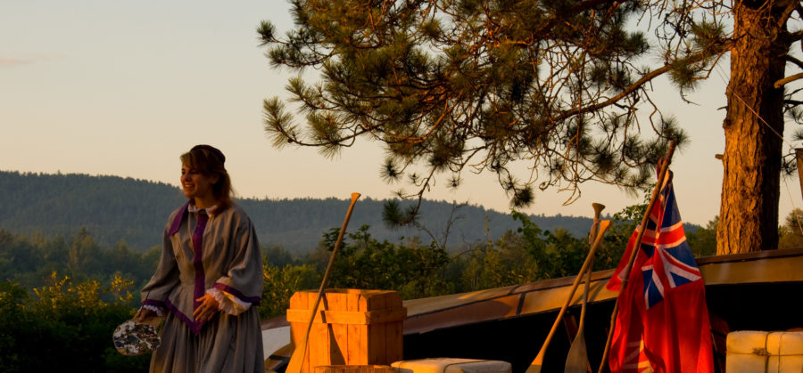 Staff member dressed in period clothing stands in front of a voyageur encampment.