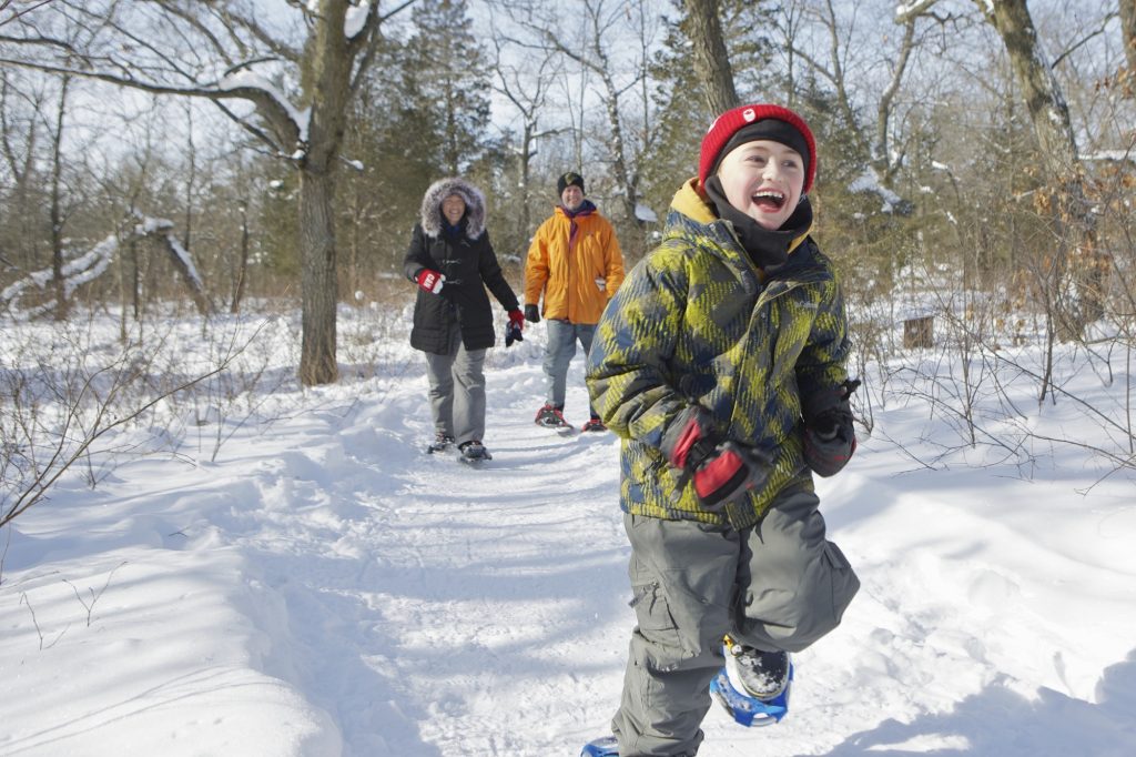 child running down winter trail with parents following
