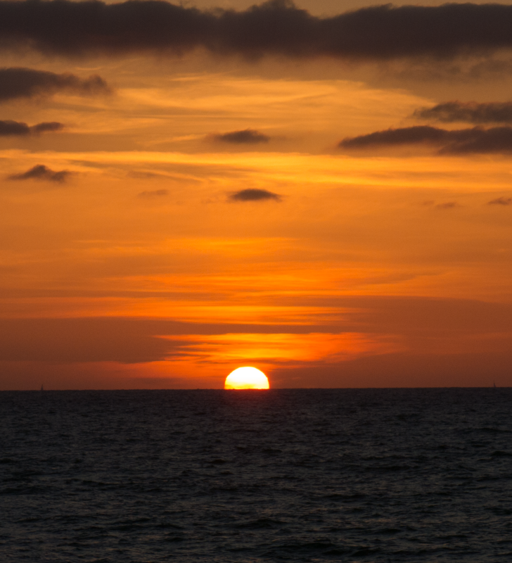 Sun setting over a lake that appears to be almost black, the sky is bright red and orange with dark clouds. 