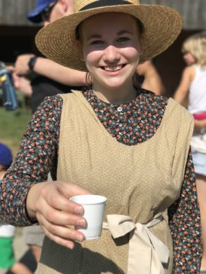 Staff member dressed in period clothing offering visitor a drink.