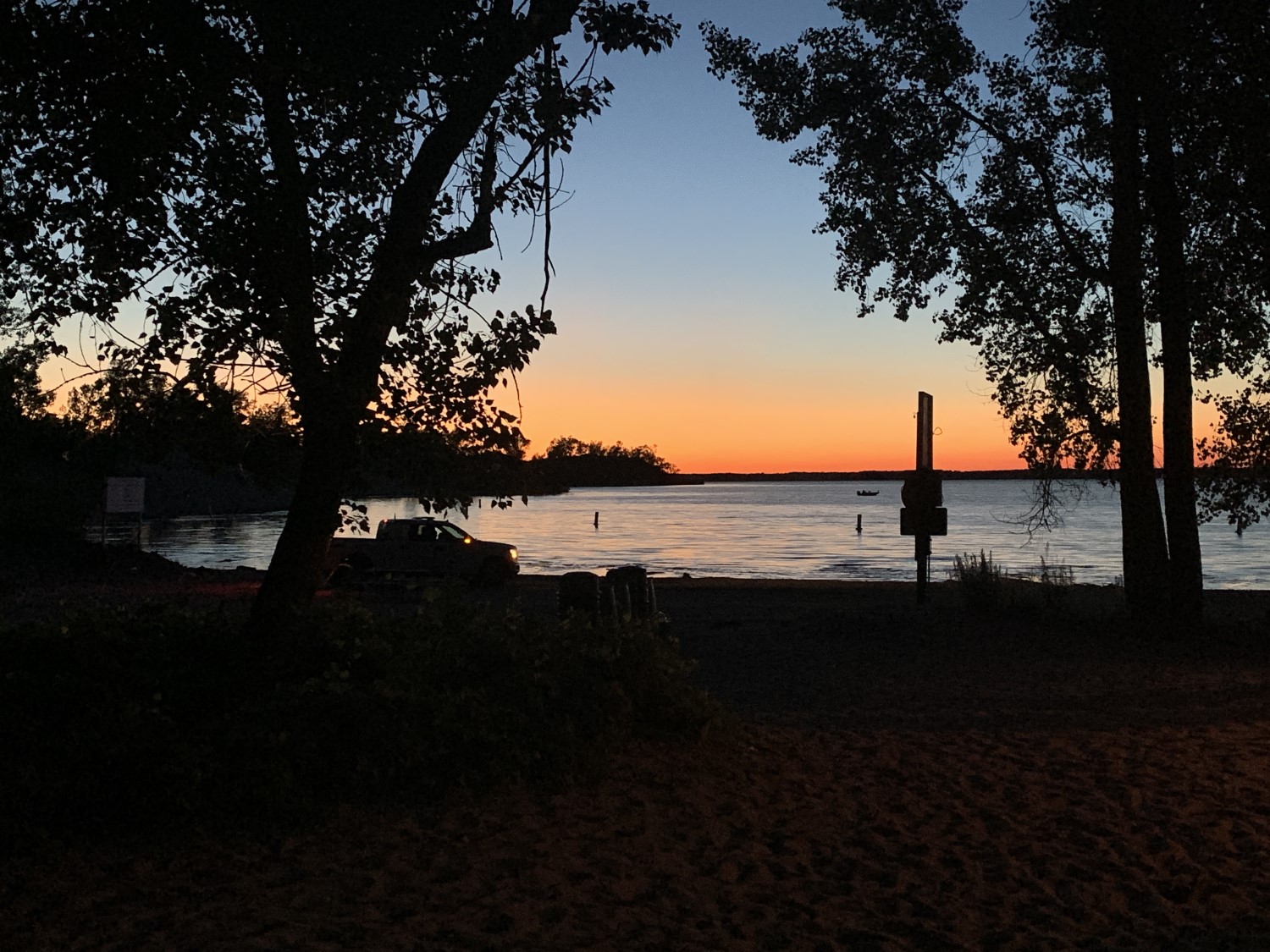 Sun setting over a lake, framed by trees in the mid distance