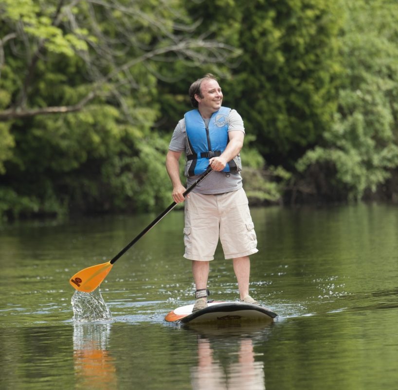 Guy paddleboarding on lake with trees in the background