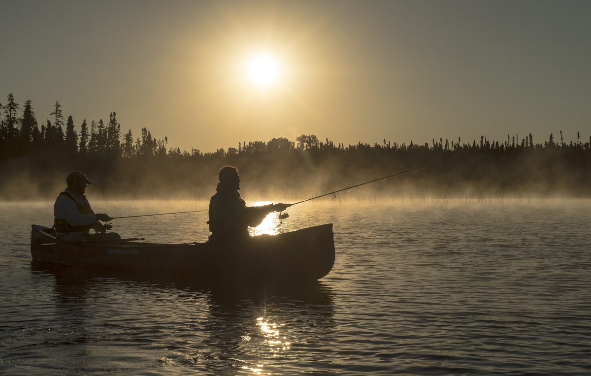 Two people fishing at sunset with mist rising off the lake and boreal forest in the background