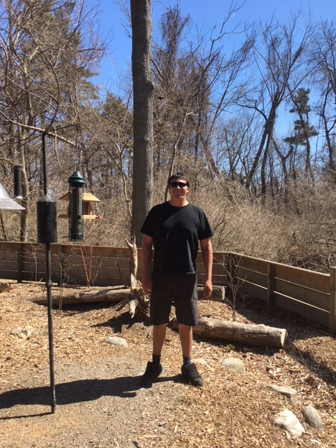 Guy in black shirt and black shorts posing on a sunny day in a natural setting in the spring