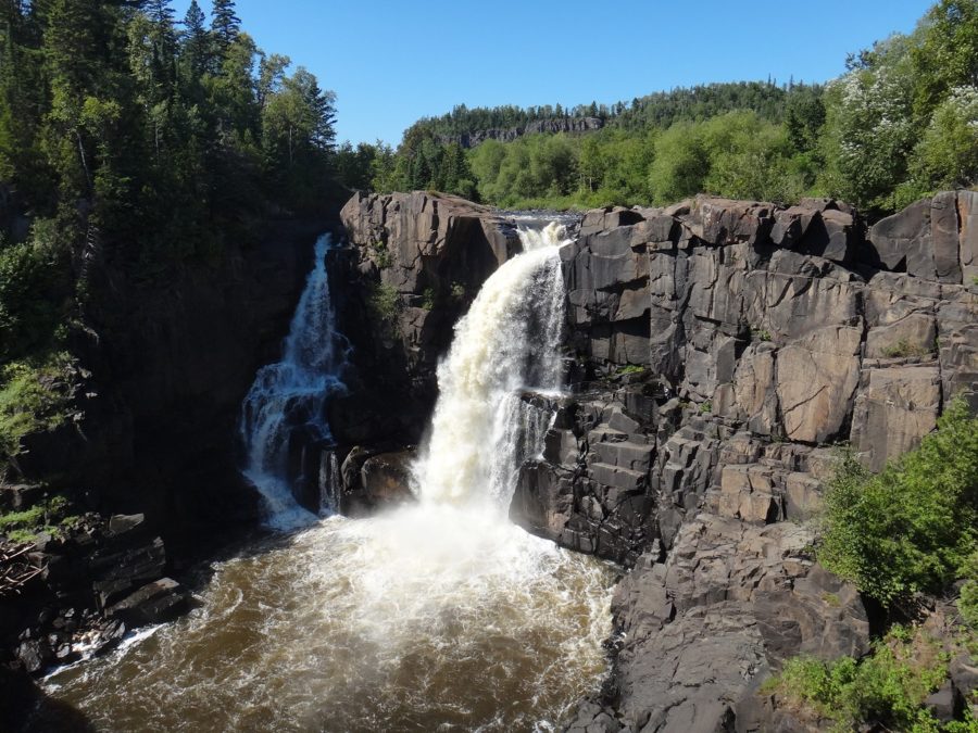 Tall waterfall on a sunny day in a primarily coniferous forest