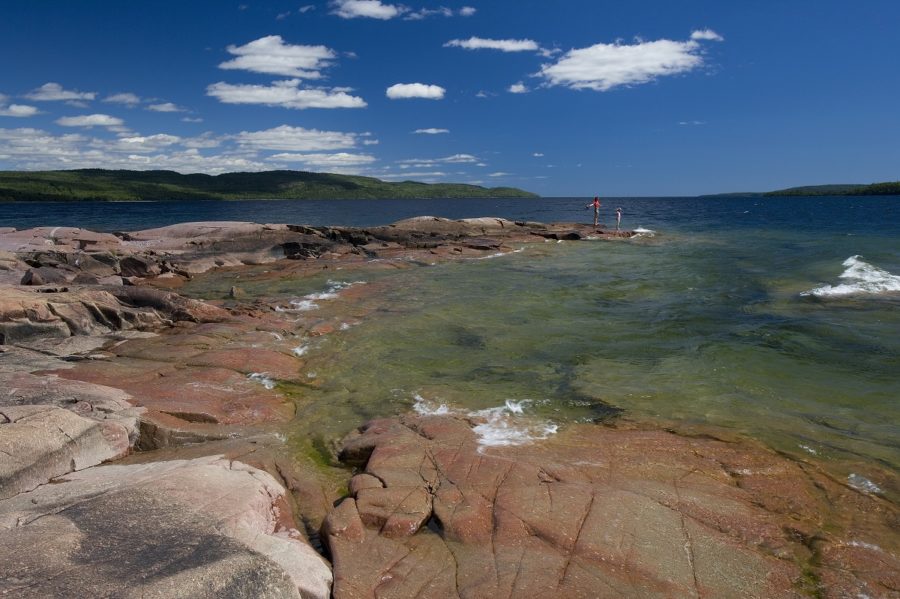 Clear green blue water with red rock shoreline, two people in the distance