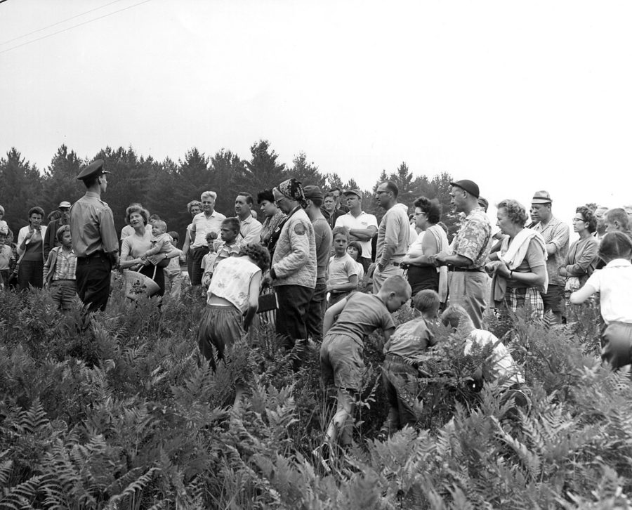 Large group of people, in a field, looking at park ranger