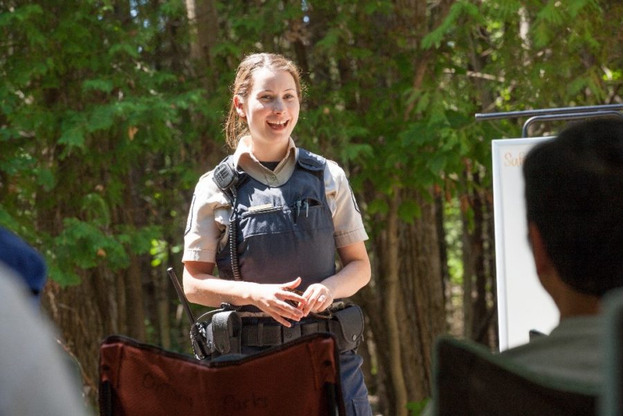 Girl with brown hair and vest addressing a group with a smile on her face