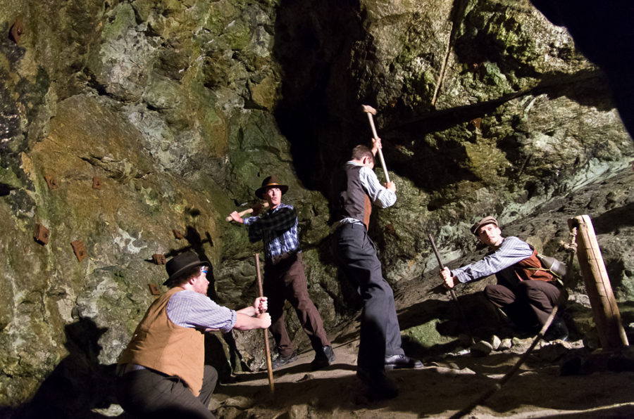 Three men in old fashioned garb with pick ax's, working in a mine