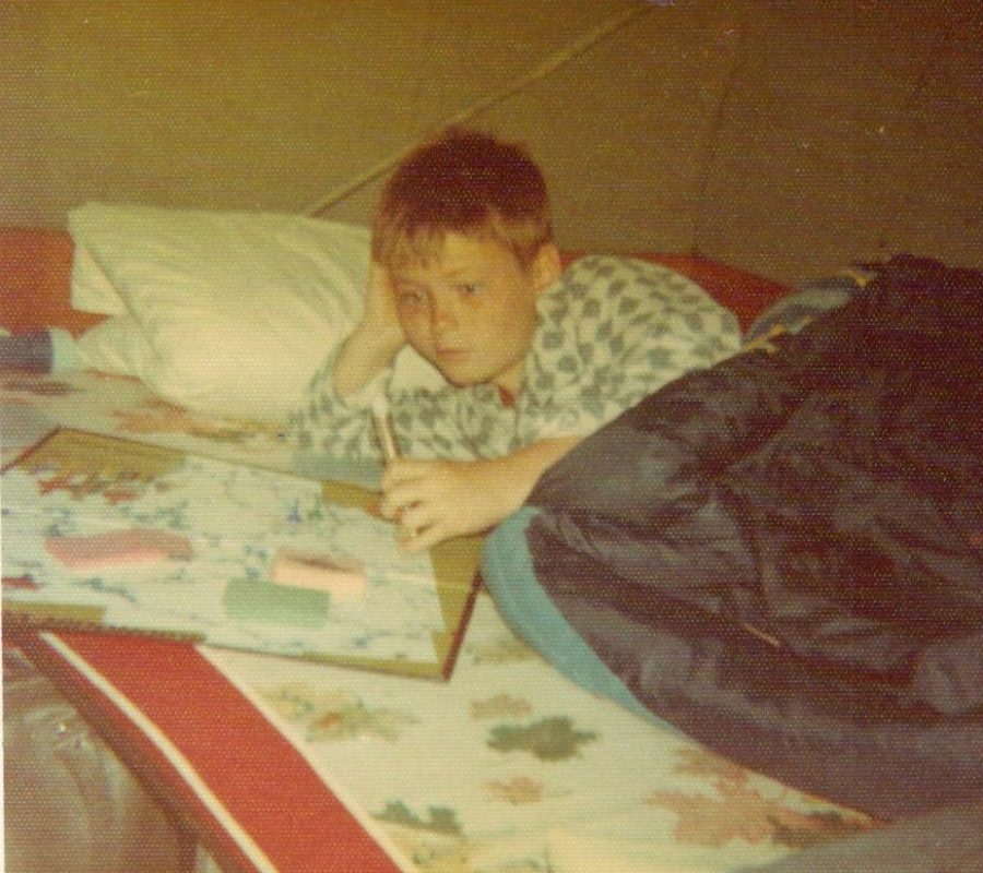 Young boy laying down in a sleeping bag, playing a board game