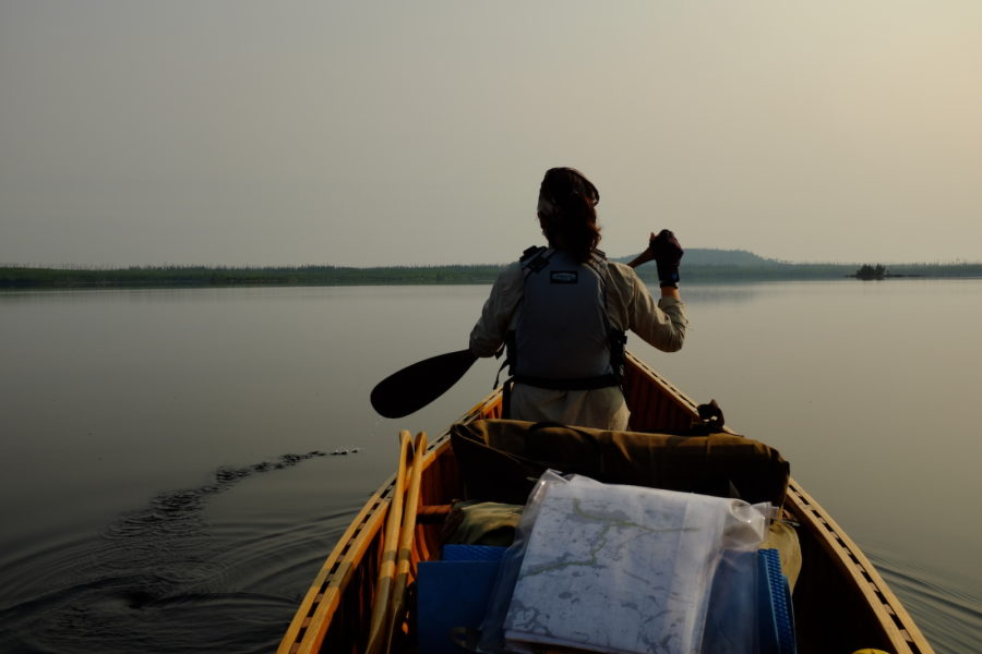 View from the back of the canoe of paddler in the front on a calm foggy lake