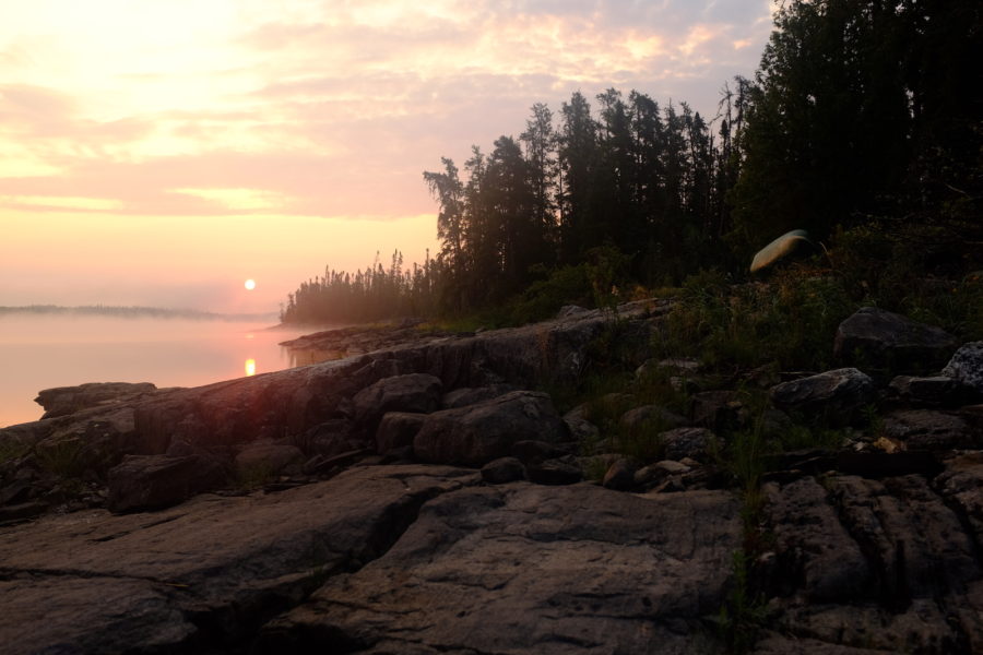 Pink sky of a low sun in the background of a rocky forested landscape