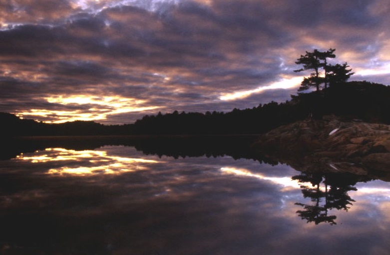 Purple and pink sky over a still lake and rocky pine shoreline