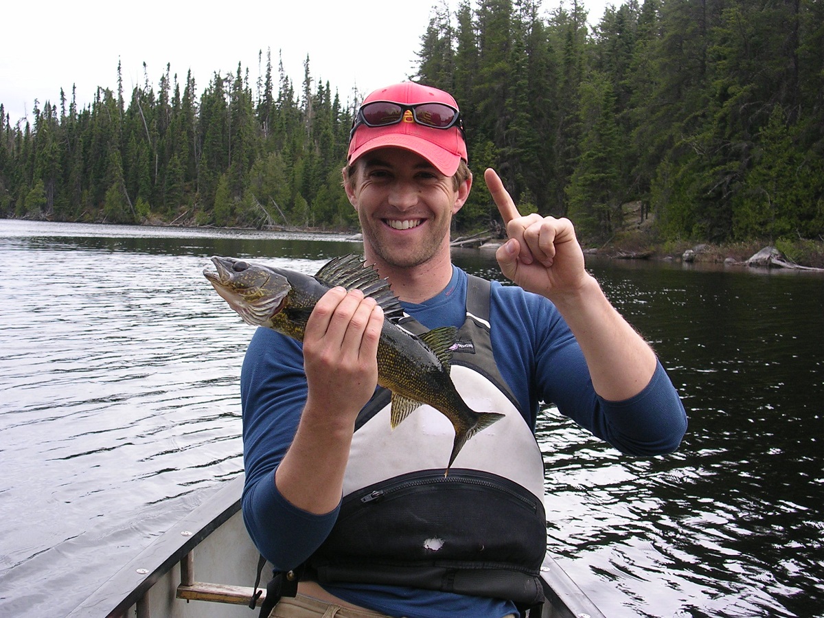 Guy with red cap holding up a walleye and his pointer finger, in a canoe