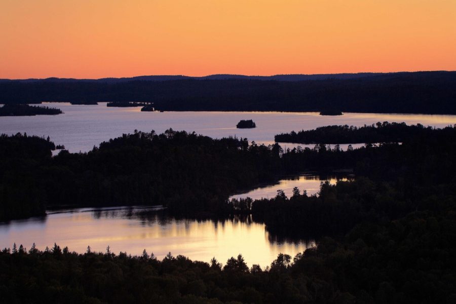 Orange sky over silhouetted forest and shining lakes